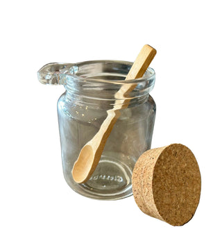 Clear glass jar with wooden spoon and cork lid on a concrete surface